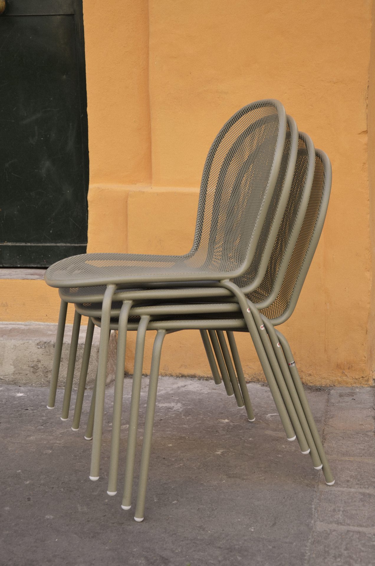 Chaises EMU empilées face au mur jaune ocre